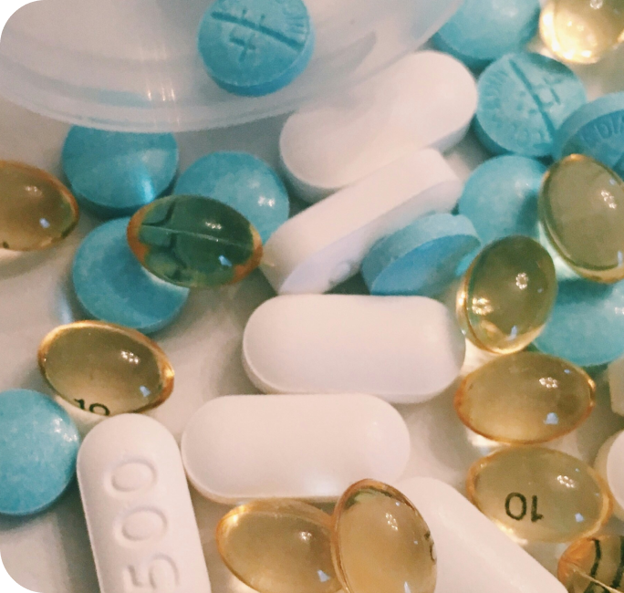 Colorful medication pills and capsules including blue tablets, white capsules, and golden gel caps